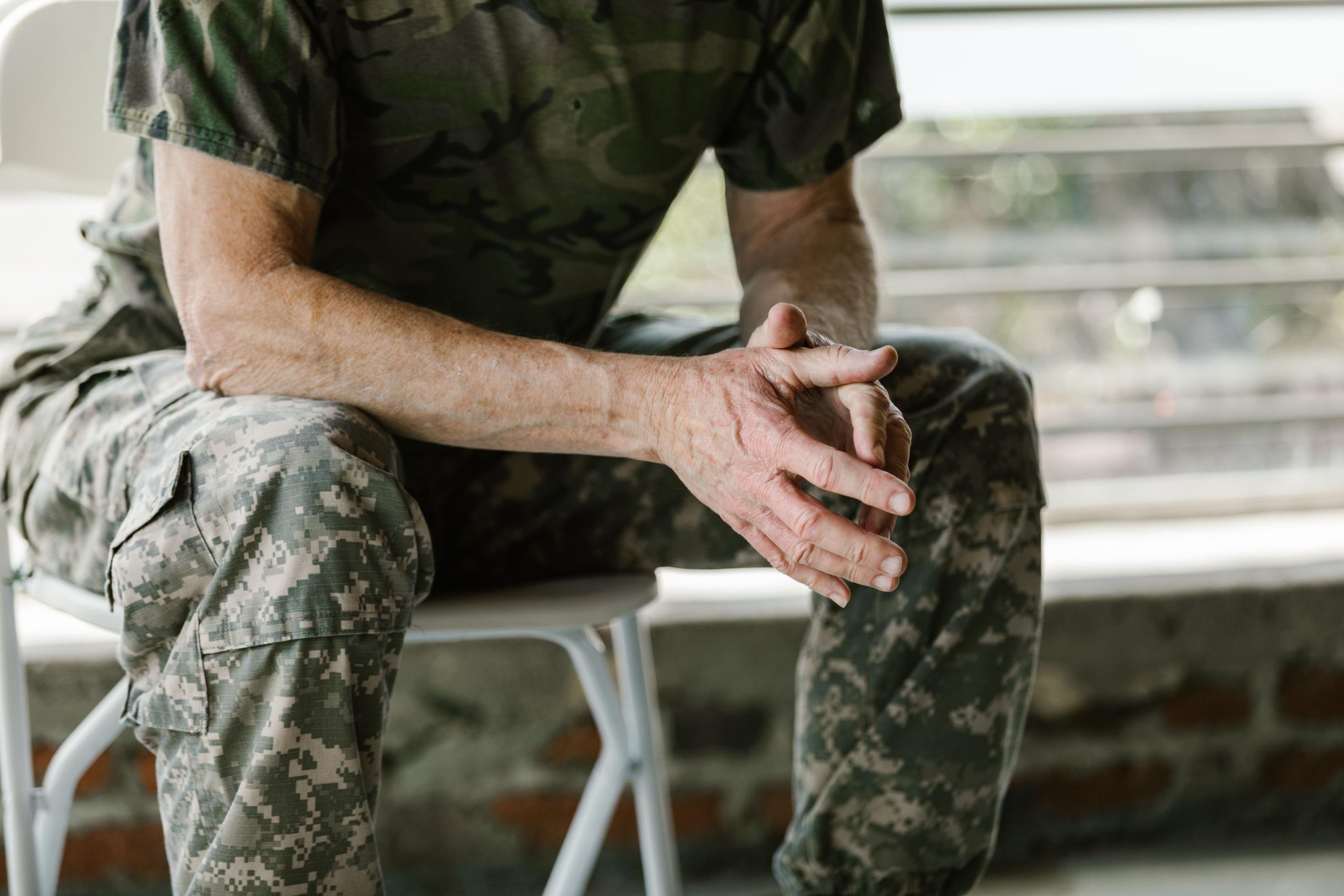 A military veteran sits with hands clasped while wearing a camouflage uniform, representing the educational and career opportunities provided through the G.I. Bill.