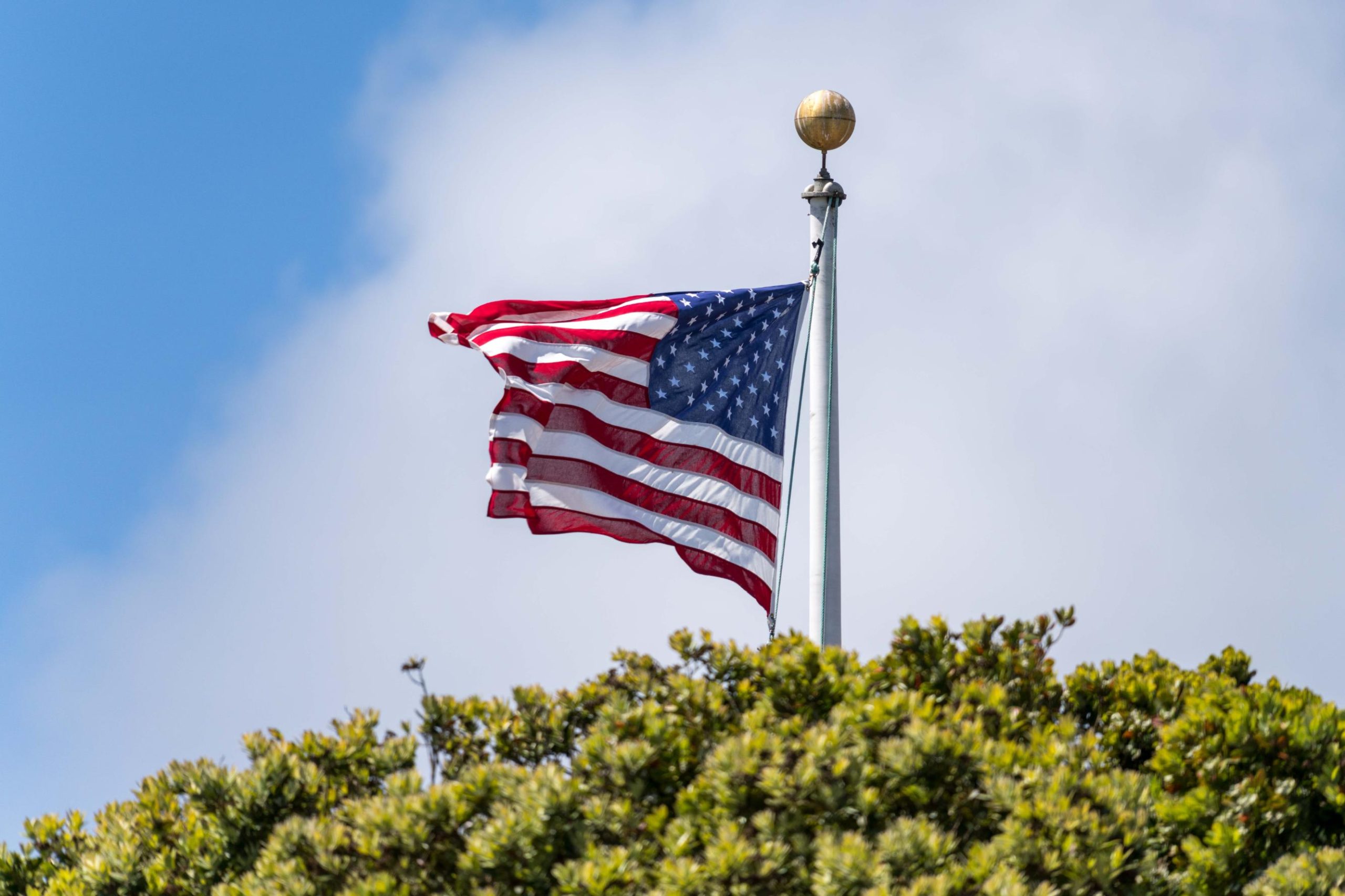 An American flag flies atop a flagpole against a blue sky, representing the United States Department of Veterans Affairs and its commitment to serving veterans and military families.