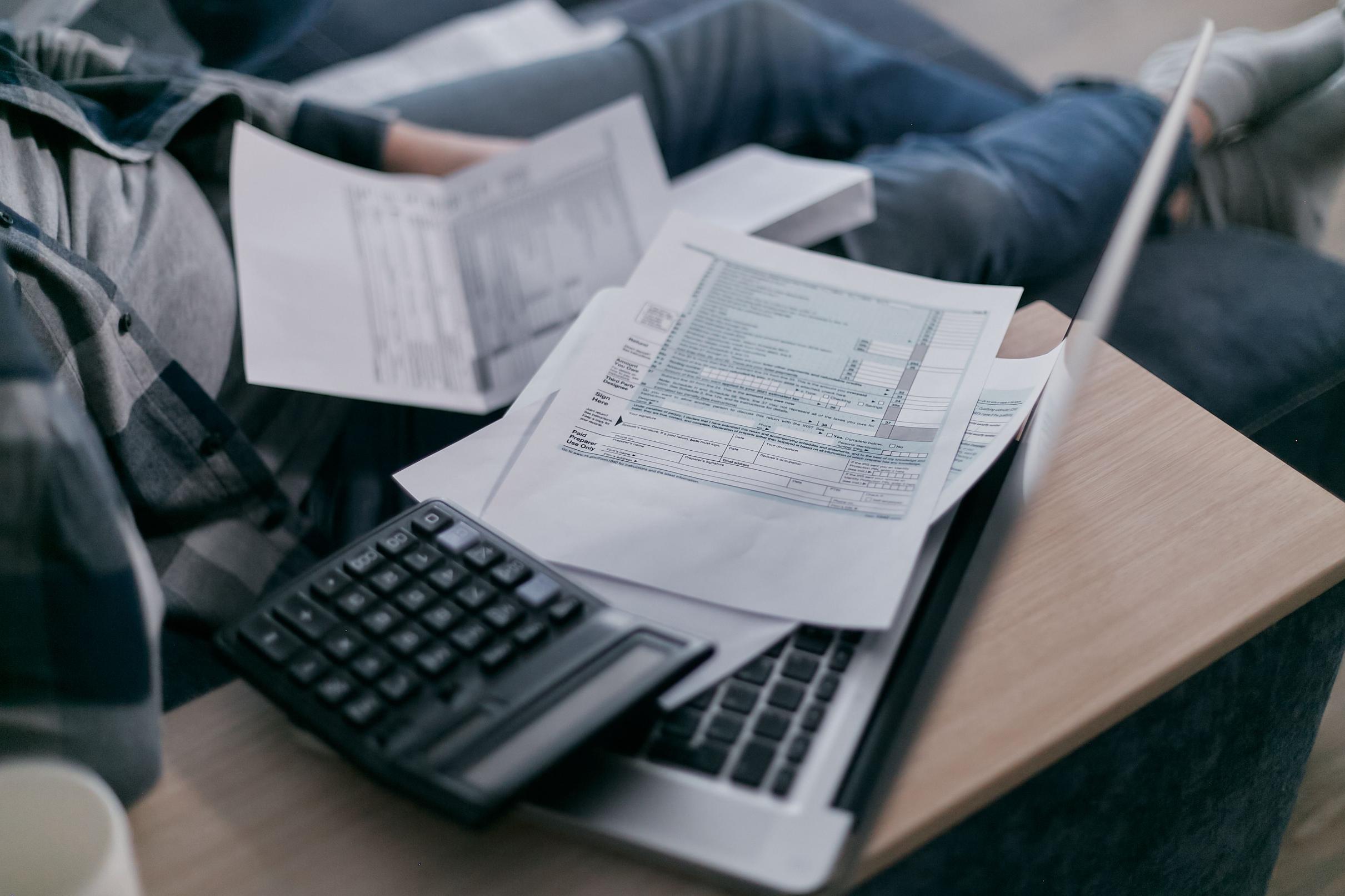 A borrower reviews financial documents with a calculator and laptop, illustrating how lenders calculate the mortgage debt-to-income (DTI) ratio during the home loan application process.