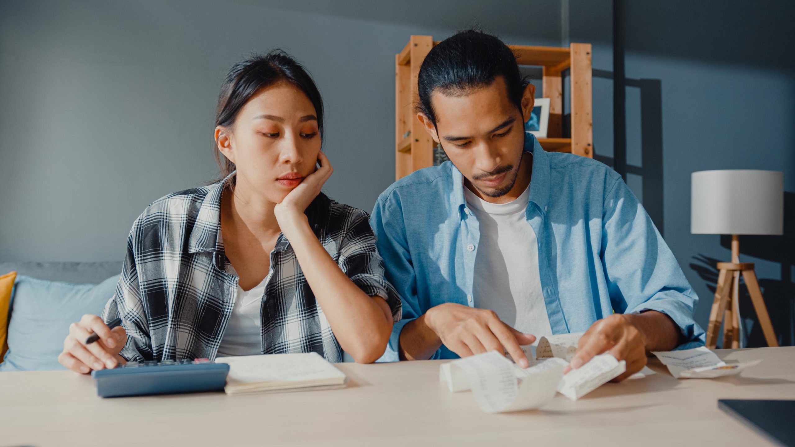 A couple reviews bills and financial documents while using a calculator, illustrating the credit and financial evaluation process for FHA loan qualification.