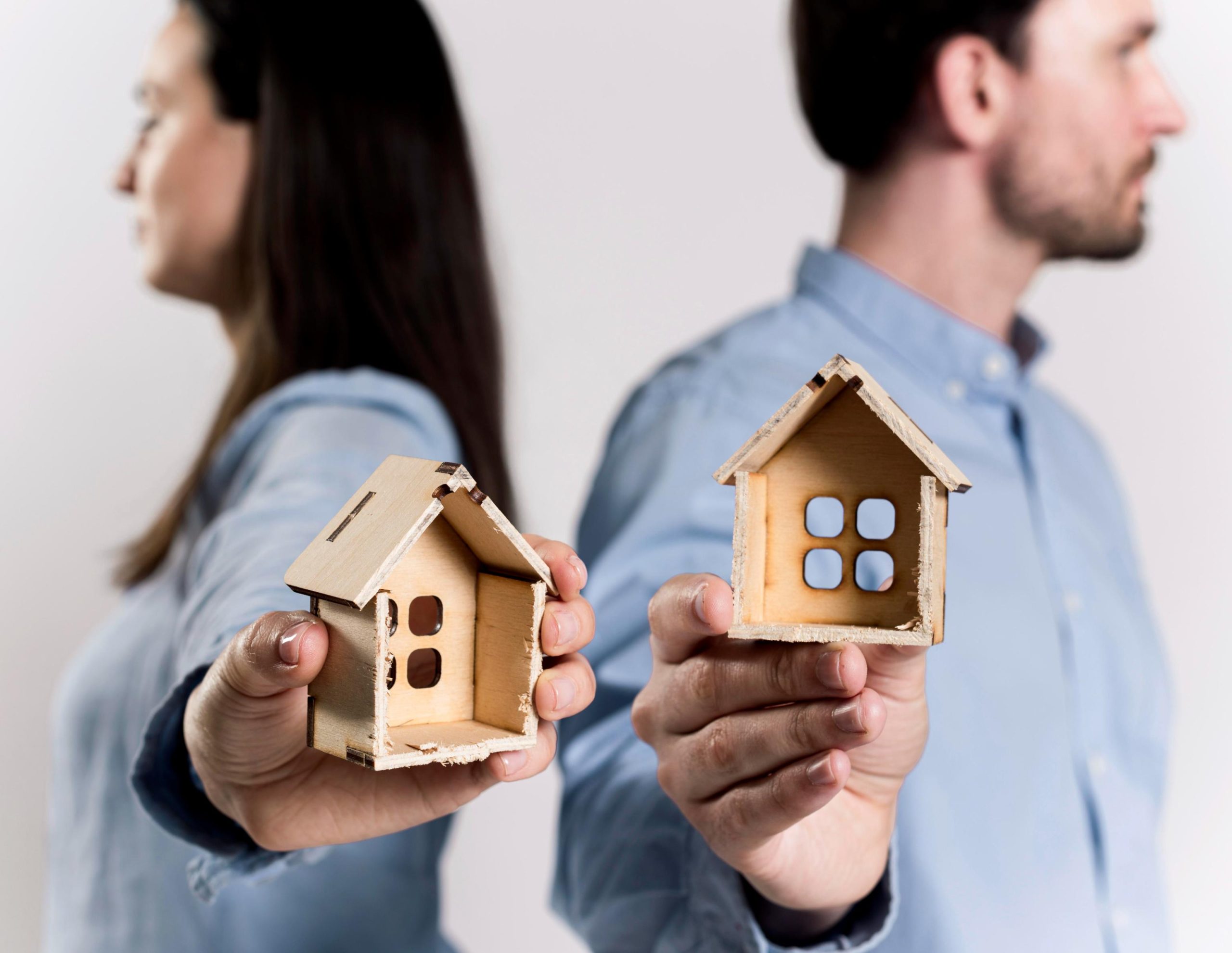 Couple holding wooden model houses while standing apart, representing jumbo home loans for purchasing or refinancing high-value properties.