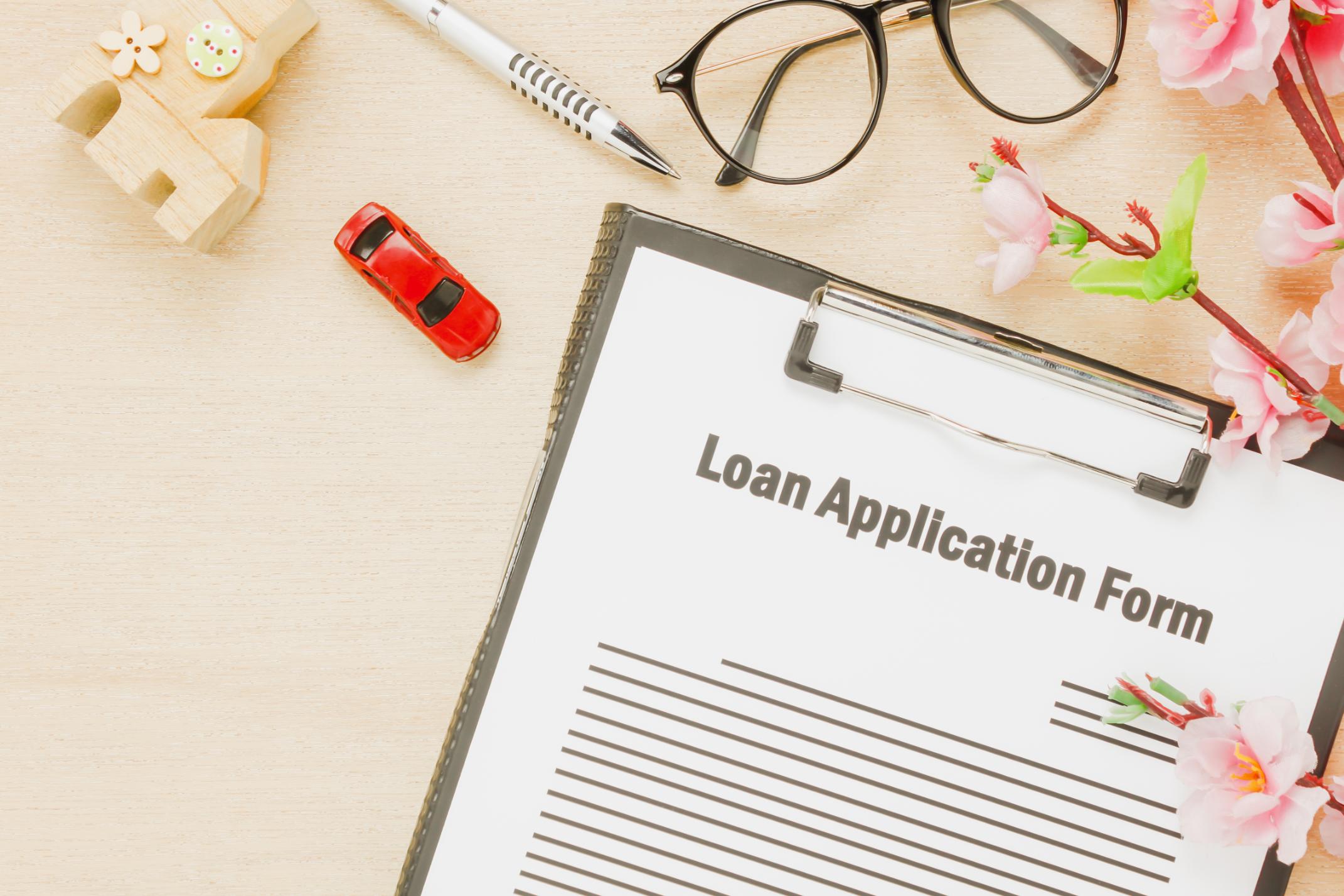 Loan application form with miniature house, toy car, and office supplies, representing the USDA Section 502 home loan program.
