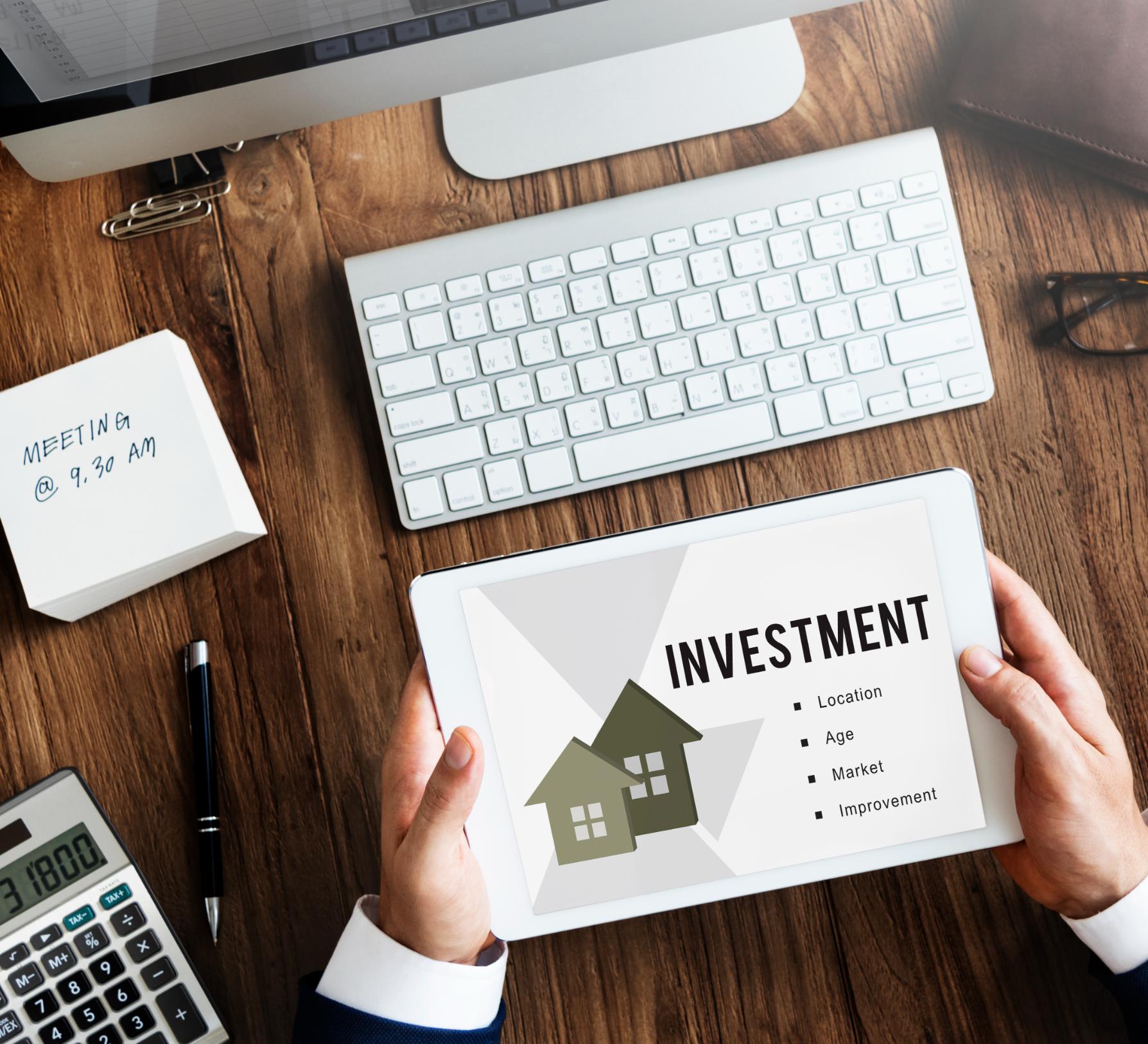 Person reviewing investment property financing options on a tablet beside a calculator, computer, and financial planning documents.