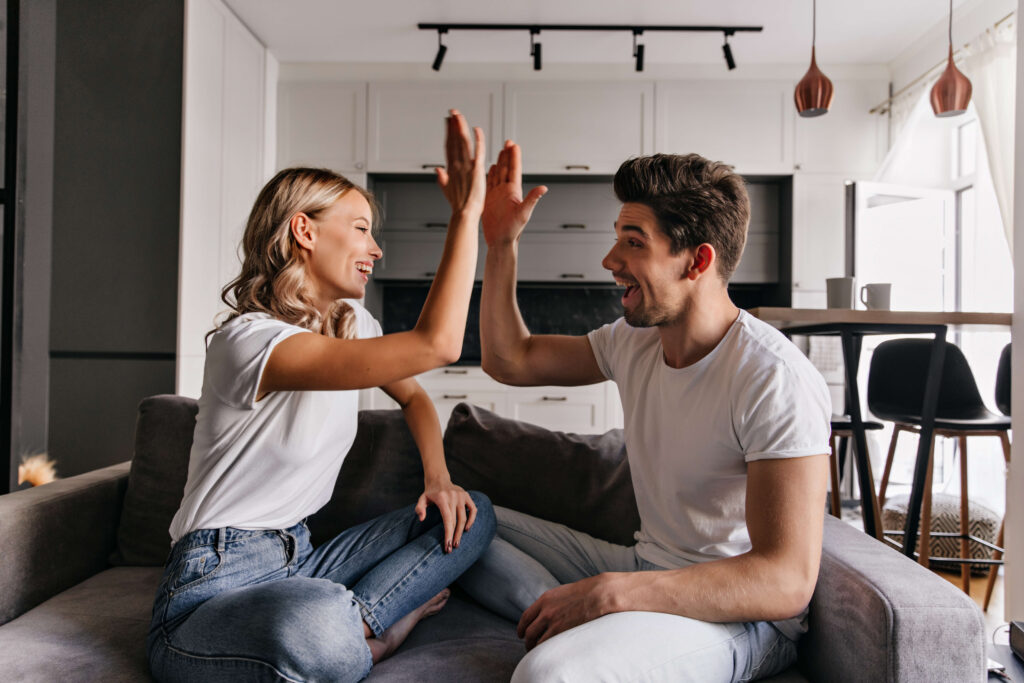 Happy couple high-fiving on the couch after a successful Texas cash-out refinance to access home equity funds.