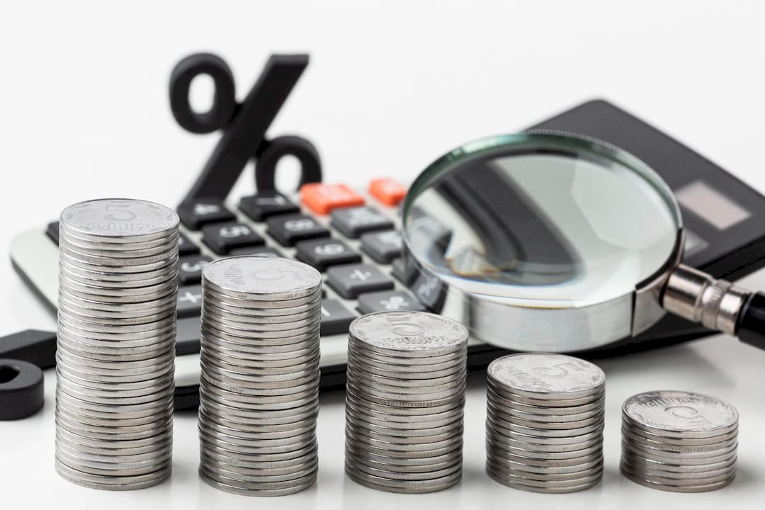 Stacks of coins beside a calculator and magnifying glass illustrating mortgage interest rates and home financing for first-time home buyers.