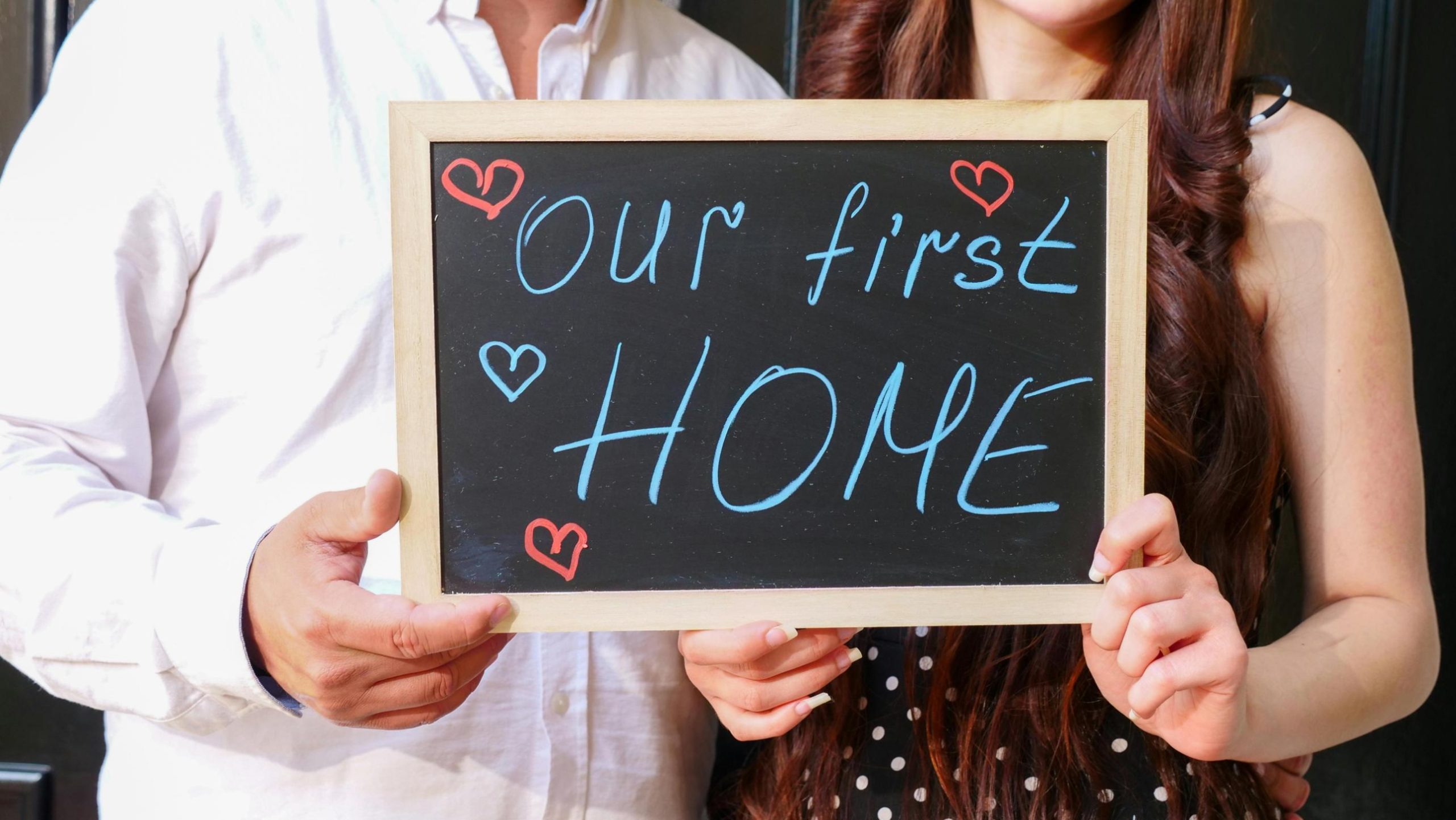Couple holding sign celebrating buying your first home in Texas with affordable mortgage options and new homeowner excitement.