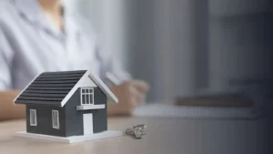 Model house with keys on a desk in front of a person reviewing mortgage paperwork, representing home financing, mortgage lending, and home buying.