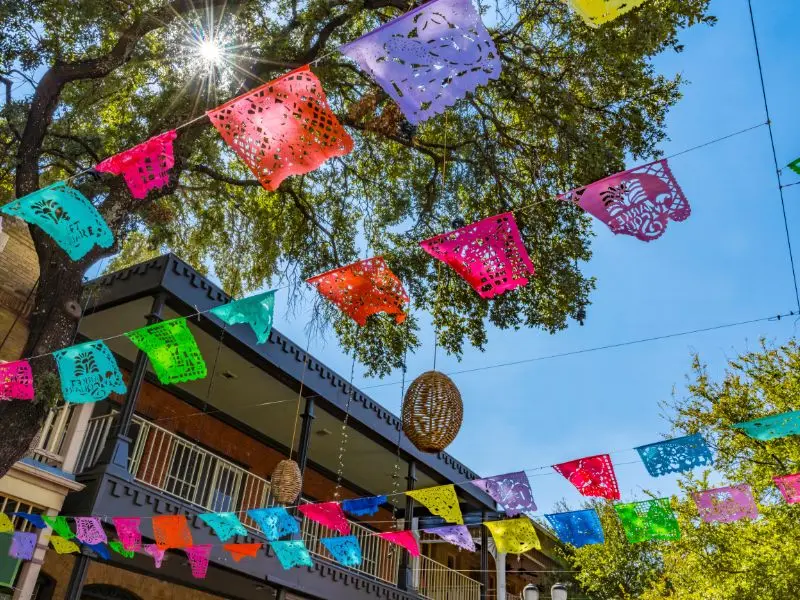 Colorful papel picado banners hanging above a street in San Antonio, Texas, celebrating the city's vibrant culture and historic downtown atmosphere.